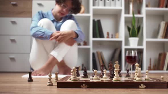A Girl A Chess Player Sits On The Floor In Front Of A Chessboard Having A Pensive Look On Her Face alt