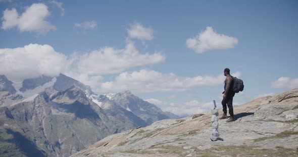 Black male traveler crossing himself and walking away from mountainside edge near the Matterhorn in alt