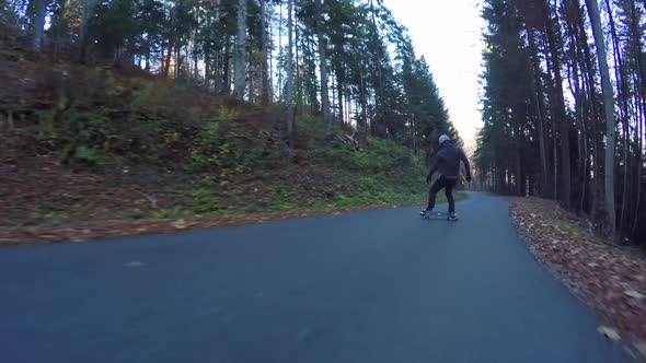 POV of young men longboard skateboarding downhill on a rural road alt