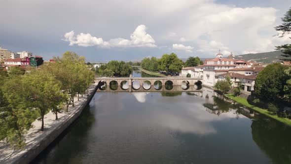 Fly over Tamega river and picturesque Roman Bridge, Chaves, Portugal. Clouds reflected on calm water alt