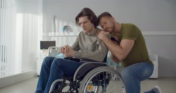 Young Man Hugging and Supporting Depressed Boyfriend in Wheelchair alt
