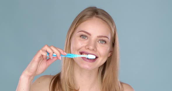 Woman with Adorable Smile Brushing Her Teeth Isolated on Blue Background