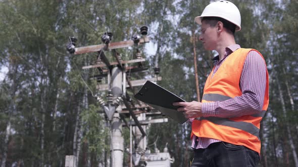 Engineer electrician check the power line, the result is written in a notebook. alt