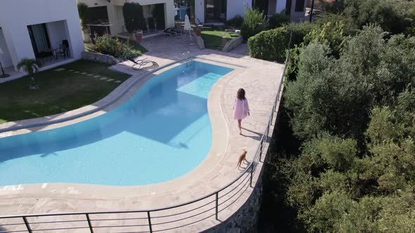 Drone footage of woman walk near swimming pool, and Modern Villas in scenic countryside. alt