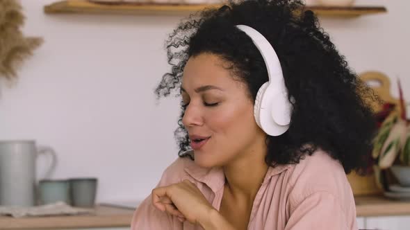 African American Woman in Big White Headphones Listens to Music with Pleasure Using Smartphone alt