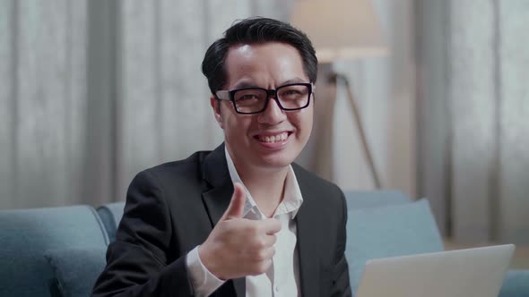 Asian Businessman In Jacket And Shorts Smiling And Showing Thumbs Up Gesture To Camera While Working alt