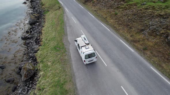 Aerial view of a camping van starting out on a journey on a road along a very calm fjord alt