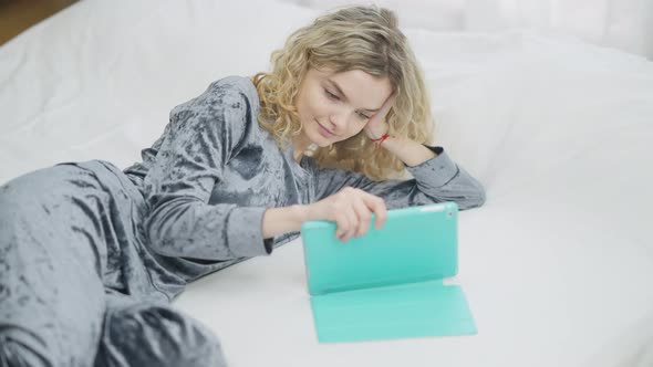 Young Relaxed Caucasian Woman Surfing Social Media on Tablet in the Morning in Bedroom alt