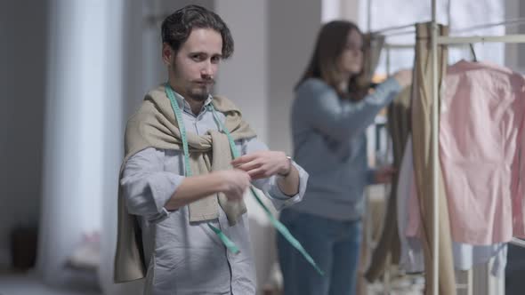 Confident Professional Fashion Designer Posing in Atelier with Client Choosing Clothes on Hanger at alt