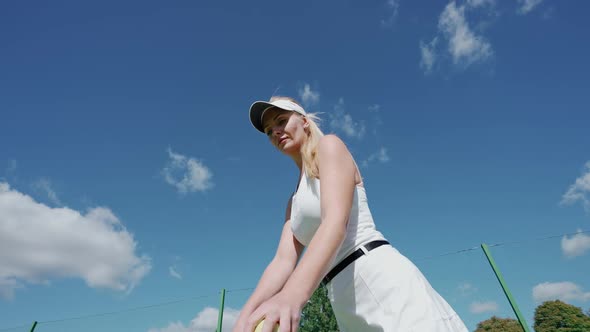 Young Woman Tennis Player Hits a Ball Off the Floor in a Outdoor Court Low Angle View Training Day alt