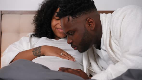 Happy Confident Young Father Kissing Pregnant Belly Listening Fetus Talking to Spouse alt