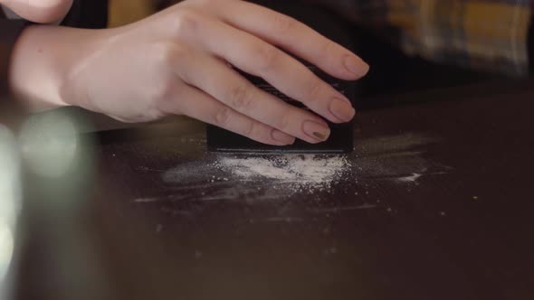 Hand of Young Drug Addict Woman Making Cocaine Line with Black Credit Card on Wooden Surface at Home alt
