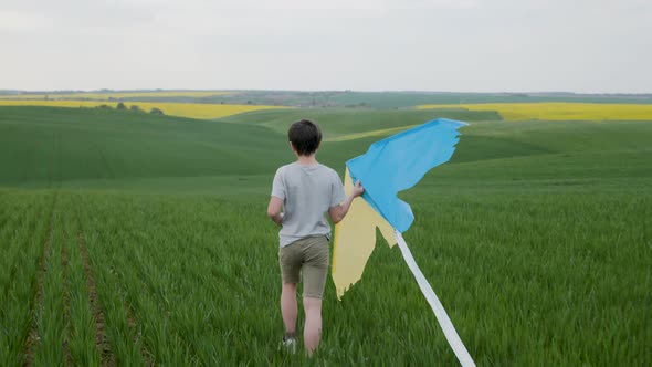 A Teenage Boy Walks Across a Field with a Yellowblue Kite