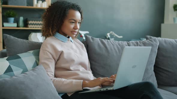 Afro-American Woman Typing with Laptop at Home Smiling and Laughing Looking at Screen alt