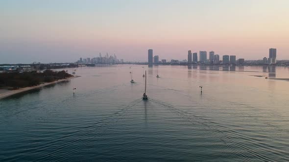 A high view of a group of yachts at sunset entering a harbour with a smoke haze city skyline in the alt