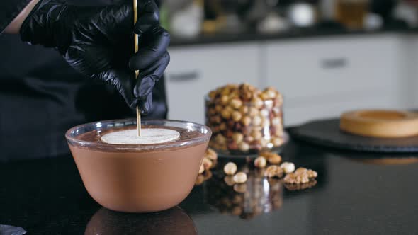 Pastry Chef is Dips a Candy in Liquid Chocolate with Nuts for Making a Cake