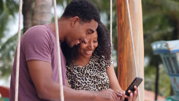 Beautiful Young African Couple Happily Watching Their Photos in a Smartphone alt