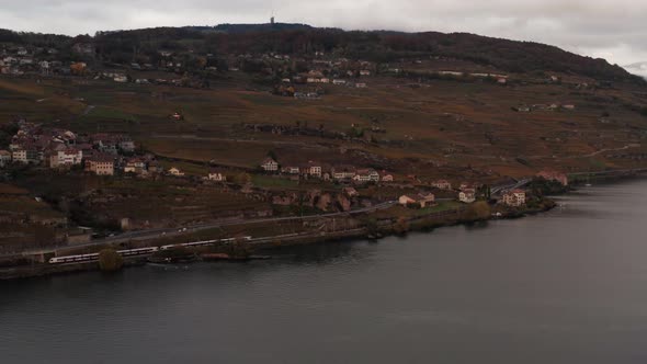 Wide aerial of train driving over railway near small village in the hills alt