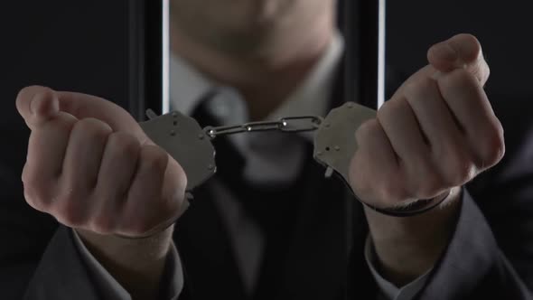 Arrested Businessman in Prison Cell Showing Handcuffs Closeup, Financial Fraud alt