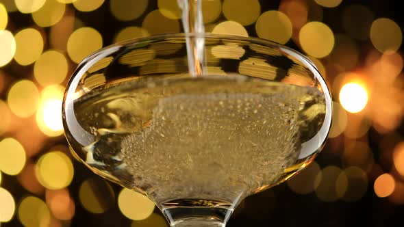 Pouring champagne into a glass against a background of golden shining lights alt