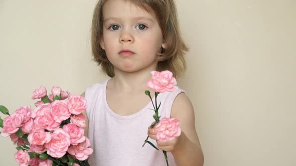 Little Girl Holds Bouquet of Flowers Pink Carnations Looks at Camera Smiles and Gives Flowers alt