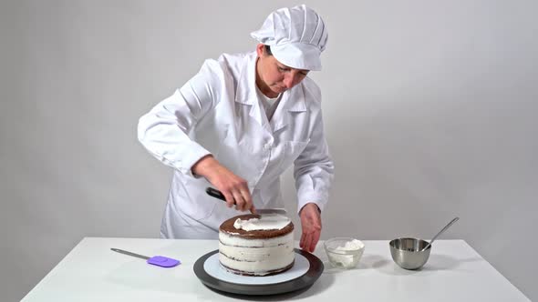 Front Shot of a Baker Using an Icing Spatula To Carefully Touch Up Sides of Cream Covered Cake alt