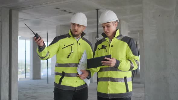 Two Engineer In Helmets With Tablet Device And Big Paper Drawings Discussing alt