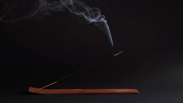The Aromatic Stick Smokes in the Stand on a Black Background. Incense for Relaxation and Meditation