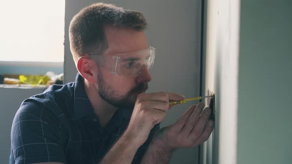 Nervous Man Repairs Plug on Wall with Screwdriver in Room alt