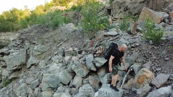 Aerial view of a young man walking along a giant rocky mountain. Traveler on the cliff. alt