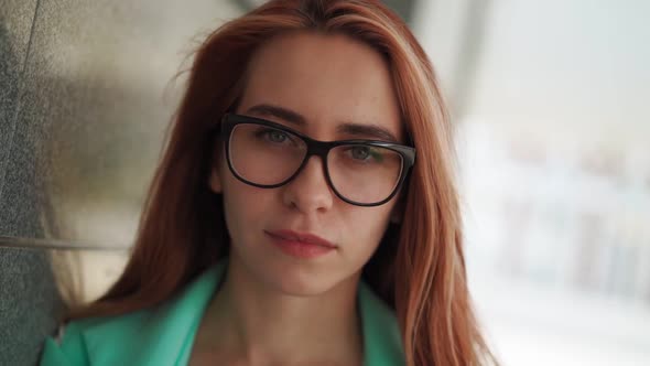 Portrait beautiful young woman in glasses with long red hair looks into camera alt