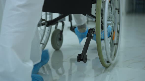 Live Camera Follows Wheel of Wheelchair with Nurse Feet in Shoe Covers Walking Along Hallway alt