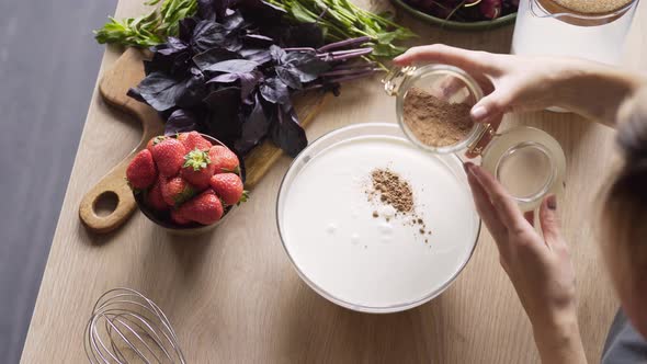 Woman Adds Cocoa Powder From Jar Into Bowl with Milk