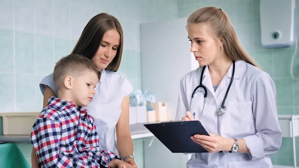 Female Doctor Using Pen Writing Complaint or Symptoms of Disease of Little Boy Patient alt
