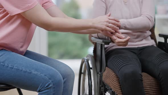 Unrecognizable Young Paralyzed Woman and Friend Holding Hands Sitting Indoors alt