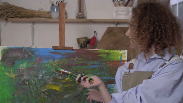 Happy Modern Artist Woman Against the Background of a Bright Abstraction Painting alt