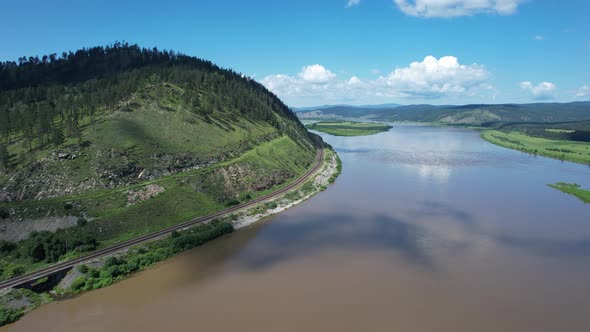 Flying Above a Glacial River in Siberia Russia with Green Mountains and Railway Track in the alt