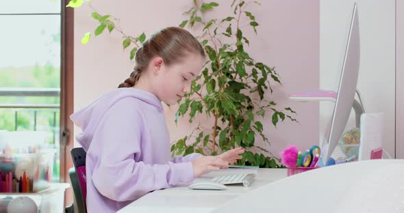 Teen Girl Typing on Keybord and Scrolling Mouse Working with Computer in Front of Monitor in Her alt