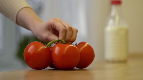 Young Woman Putting Fresh Vegetables Tomatoes and Onions on Table in Kitchen
