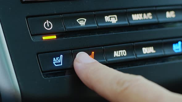 A woman presses the gray seat warmer button in a modern car in close-up
