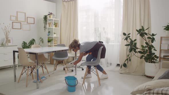 Woman Mopping Floor under Chairs in Living Room alt