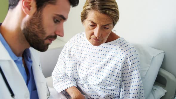 Male doctor discussing medical report with female patient on digital tablet alt