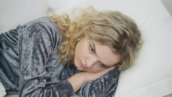 Closeup of Sad Beautiful Young Caucasian Woman Lying in White Bed Thinking alt