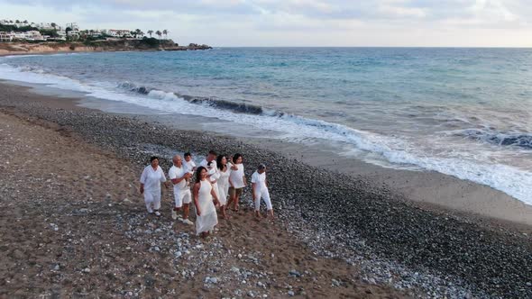 Happy Multigenerational Family Strolling on Picturesque Mediterranean Sea Beach Waving at Sunset alt