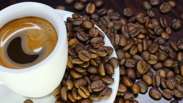 A Cup of Hot Coffee with Roasted Beans Around on a Black Background in  Resolution in Slow Motion