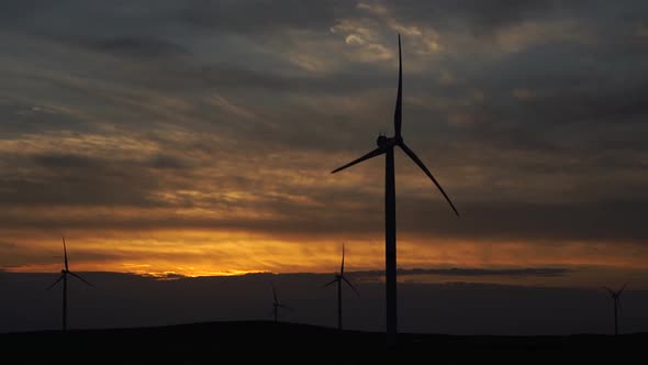 Motion the Blades of a Large Wind Turbine in a Field Against a Background of Orange Sunset on the alt