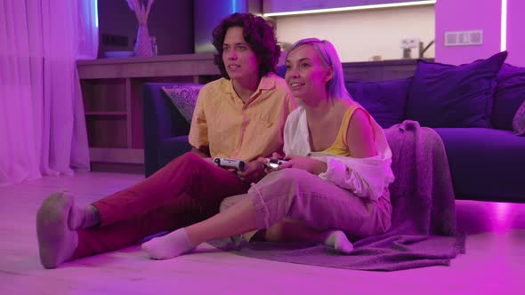 Two Happy Friends Playing Action Video Game in the Living Room Sitting on the Sofa alt