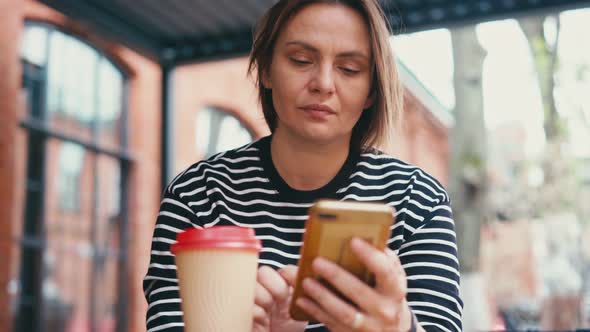 A Young Adult Woman Sits on an Open Veranda and Uses Her Smartphone alt