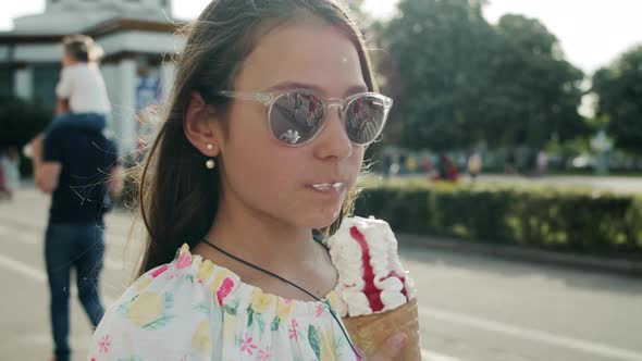 Pretty Girl Eating Ice Cream Cone. Relaxed Teen Girl Walking in Amusement Park alt