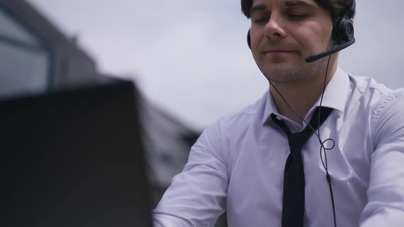 Handsome Brunette Man Putting on Headphones Texting on Laptop Sitting Outdoors alt